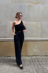 a lady in a black asymmetrical top and a pair of black pleated pants